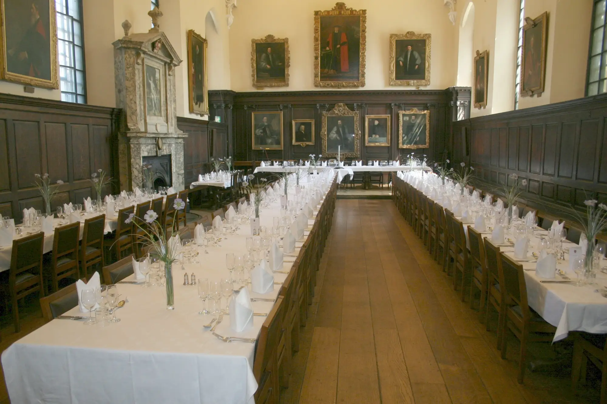 The Main Hall at St John's College: dark oak panelling hung with gilt-framed portraits, a carved stone fireplace, and long tables laid with white linen and glassware.
